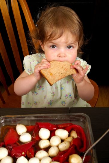 very-young-girl-seated-at-the-dinner-table-eating-a-slice-of-whole-wheat-bread-364x544.jpg